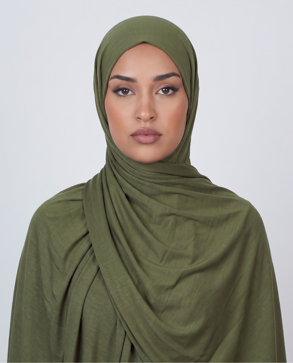 A woman wearing an olive green draped hijab, photographed against a clean light gray studio background.
