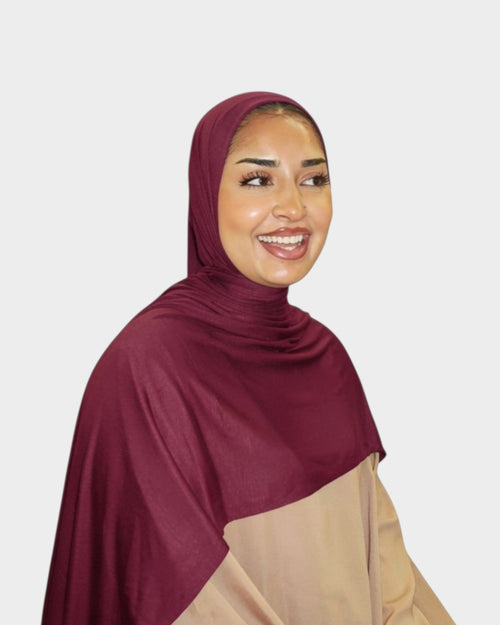 HIJABI LONDON burgundy premium jersey hijab draped on a smiling woman. Soft, breathable fabric with versatile styling.